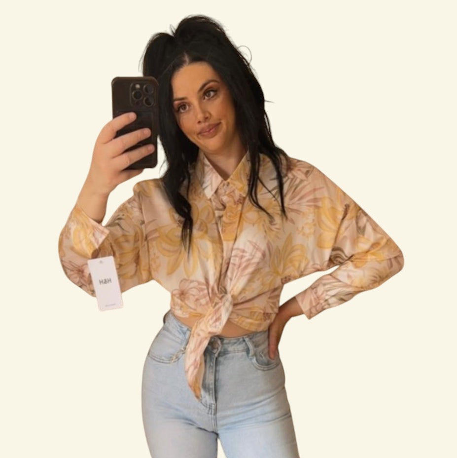 PINTONAS camisa satinada de manga larga con estampado floral en tonos pastel y amarillo, anudada a la cintura.
