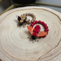PINTONAS pulsera con cuentas marrones y rojas, adornada con un insecto de resina y metal con alas naranjas.