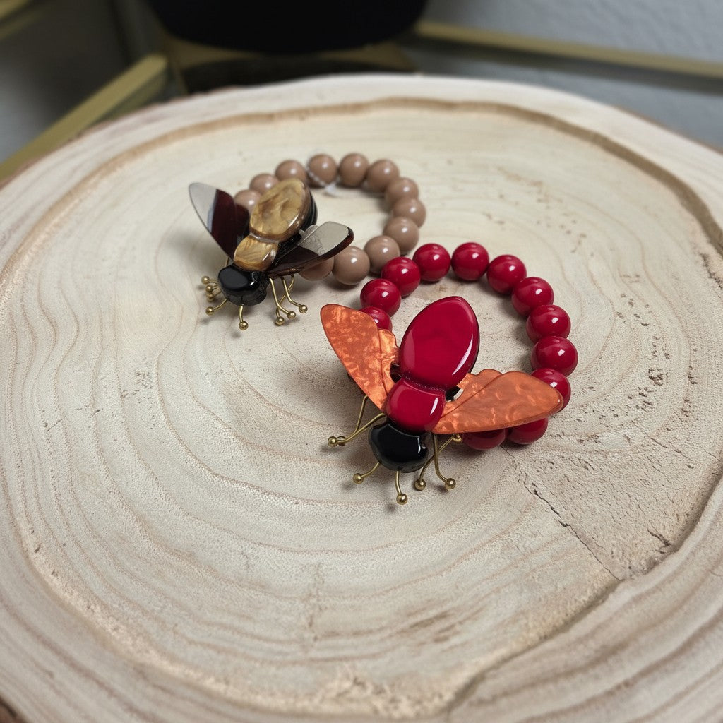 PINTONAS pulsera con cuentas marrones y rojas, adornada con un insecto de resina y metal con alas naranjas.