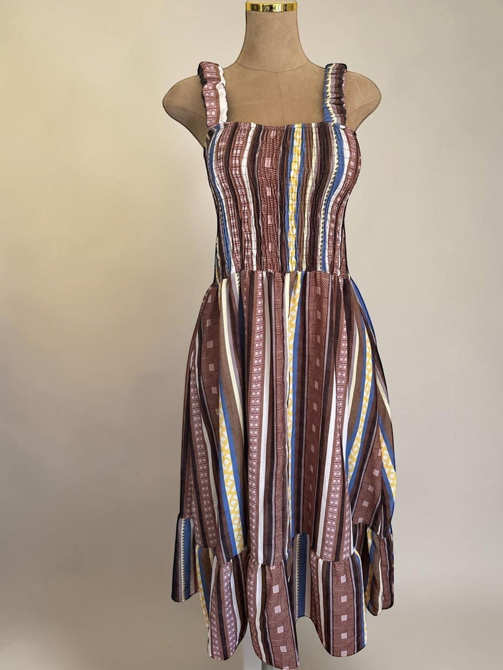 PINTONAS vestido midi de rayas verticales en tonos marrones, azules y amarillos. Cuerpo fruncido nido de abeja y falda con volante.