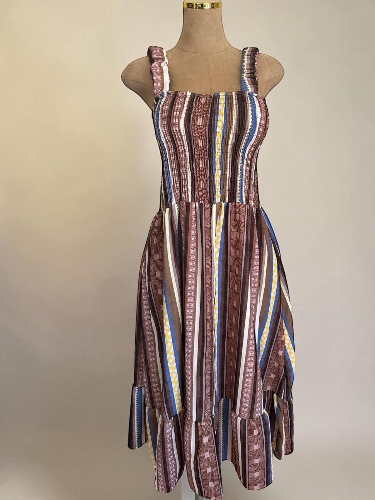 PINTONAS vestido midi de rayas verticales en tonos marrones, azules y amarillos. Cuerpo fruncido nido de abeja y falda con volante.