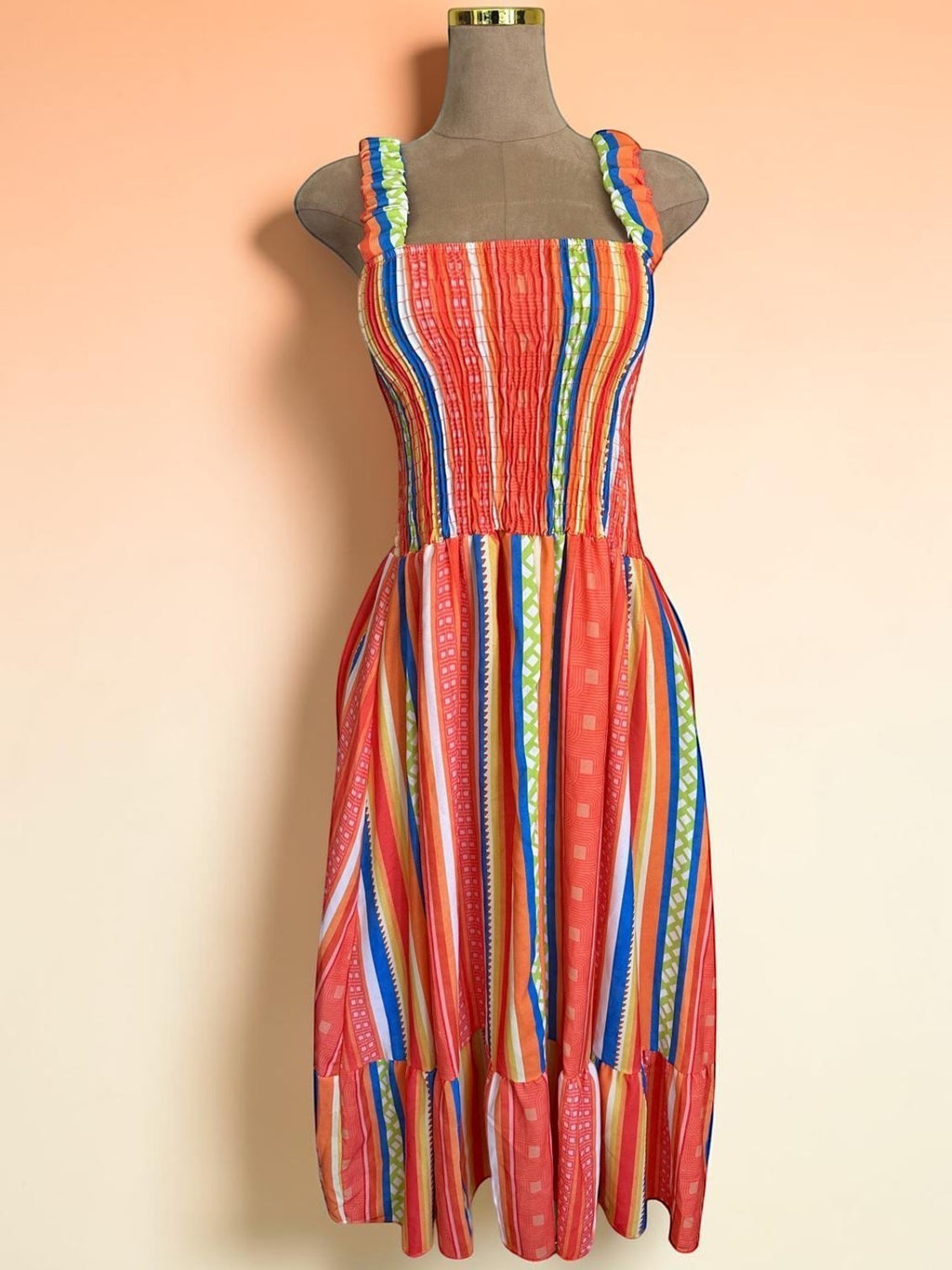 Vestido midi PINTONAS de rayas verticales en naranja, azul y verde. Cuerpo fruncido nido de abeja y falda con volante. 50% Viscosa / 50% Poliéster.